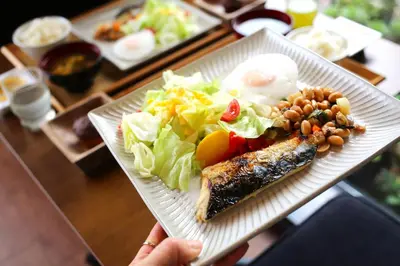 a person holding a white plate with a salad and fish at Tabist TOKYO CITY VIEW HOTEL in Tokyo