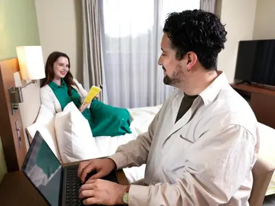a man sitting in a bed with a laptop with a woman at Tokyu Stay Monzen-Nakacho Tokyo in Tokyo