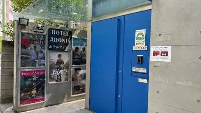 a blue door on the side of a building with posters at Hotel Adonis Tokyo - Dormitory Share Room For Male Only At City Center in Tokyo