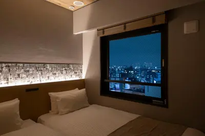 a bedroom with two beds and a window with a city at HOTEL AMANEK Kamata-Eki Mae in Tokyo