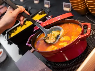 a person stirring a pot of soup with a spoon at Super Hotel Premier Akihabara in Tokyo