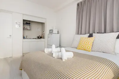 a white bedroom with a bed with a refrigerator at Hotel Apartment Ueno Inaricho Sta in Tokyo