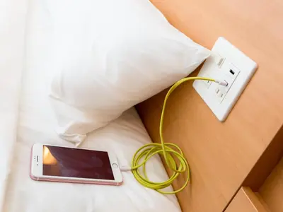 a cell phone with a cord plugged into an outlet on a bed at Super Hotel Tokyo JR Shinkoiwa in Tokyo
