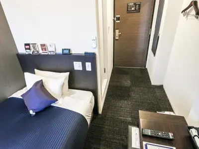 a bedroom with a bed with a blue pillow and a hallway at HOTEL LiVEMAX Shinjuku EAST in Tokyo