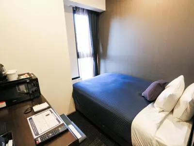 a hotel room with a bed and a desk with a phone at HOTEL LiVEMAX Shinjuku EAST in Tokyo