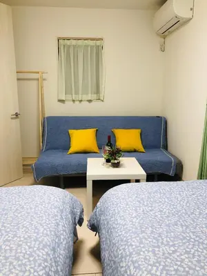 a room with two beds and a couch with yellow pillows at Takara House in Tokyo