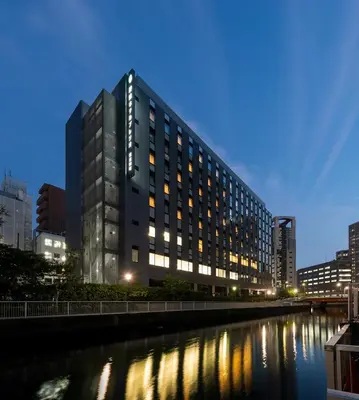 a tall building next to a river at night at Shizutetsu Hotel Prezio Tokyo Tamachi in Tokyo
