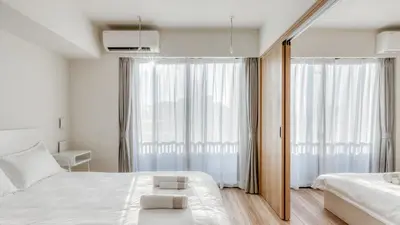 a white bedroom with two beds and a window at Ostay Nippori Hotel Apartment (Nishi-Nippori Sta.) in Tokyo