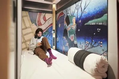 a person sitting on a bed in front of a wall at Resol Poshtel Tokyo Asakusa in Tokyo