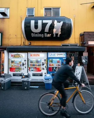 a man riding a bike in front of a drinking bar at illi Sun Shimokitazawa in Tokyo