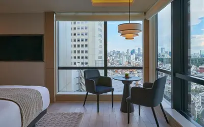 a bedroom with a bed and chairs and a window at Kimpton Shinjuku Tokyo by IHG in Tokyo