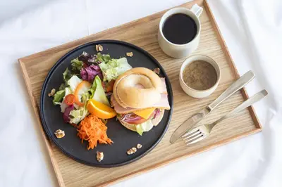 a black plate with a sandwich and salad and a cup of coffee at KAIKA Tokyo by THE SHARE HOTELS in Tokyo