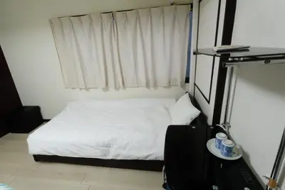 a small bedroom with a white bed and a suitcase at Tokyo Kakan in Tokyo
