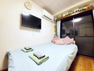 a bedroom with a white bed with a tv on the wall at nestay suite tokyo tabata in Tokyo