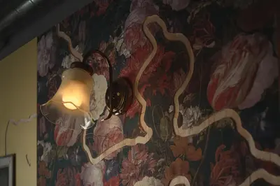 a lamp on a wall with a floral wallpaper at BnA WALL in Tokyo