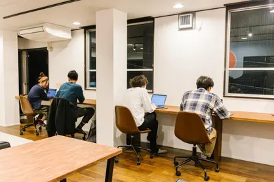 a group of men sitting at a desk with laptops at unito CHIYODA in Tokyo