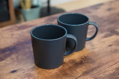 two black coffee mugs sitting on a wooden table at H.W.HILLS.103 in Tokyo