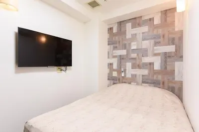 a bedroom with a bed and a tv on a wall at Otsuka Town Hotel in Tokyo