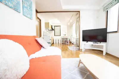 a living room with an orange couch and a flat screen tv at Elle's Shirokane Guest house in Tokyo
