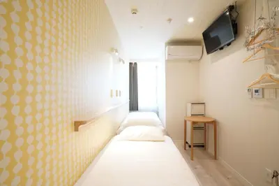 a room with three beds and a tv on a wall at U-Hotel Takadanobaba in Tokyo