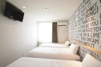 two beds in a room with a wall with writing on it at U-Hotel Takadanobaba in Tokyo