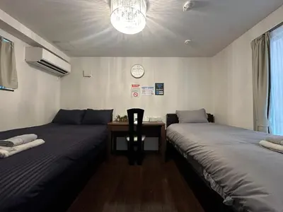 two beds in a room with a desk and a clock at nestay house tokyo shinjuku in Tokyo