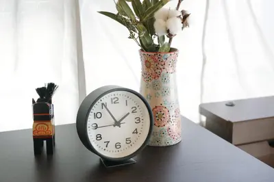 a clock on a table next to a vase with flowers at Villa Belle-Vue Kanegafuchi in Tokyo