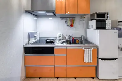 a kitchen with orange cabinets and a white refrigerator at Diamond Moon Palace Takadanobaba,2 stops to Shinjuku in Tokyo