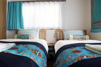 a room with two beds and a window with blue curtains at HAMA HILLS Shinjuku in Tokyo