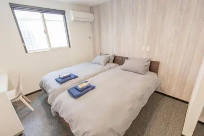 two twin beds in a room with a window at Port House Hatsudai in Tokyo