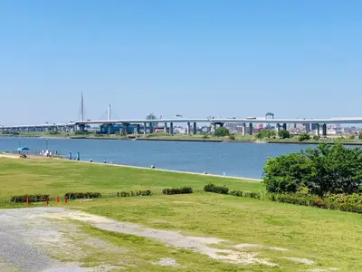 a grassy field next to a river with a bridge in the background at Green House 101 in Tokyo