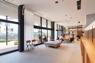 a lobby with people sitting at tables and windows at MUSTARD HOTEL SHIMOKITAZAWA in Tokyo