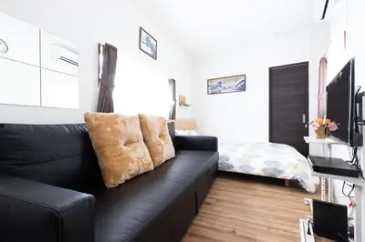 a living room with a black couch and a bed at Peace Inn Skytree Tokyo in Tokyo