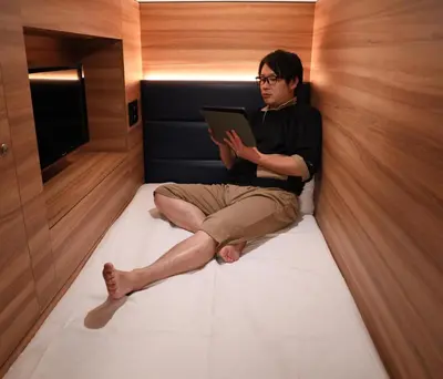 a man sitting on a bed with a tablet at Smart Stay SHIZUKU Shinagawa-Oimachi in Tokyo