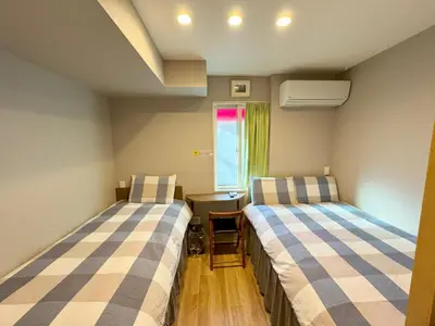 two beds in a room with a table and a window at SHINJUKU WARM HOUSE in Tokyo