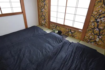 a bedroom with a bed with a blue comforter and two windows at Sasatsuka Fleur Tachibana Hotel Apartment in Tokyo