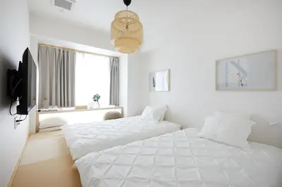 two white beds in a white bedroom with a window at Designers Hotel Siesta in Tokyo