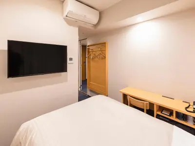 a bedroom with a bed and a desk and a tv at Sotetsu Fresa Inn Daimon in Tokyo