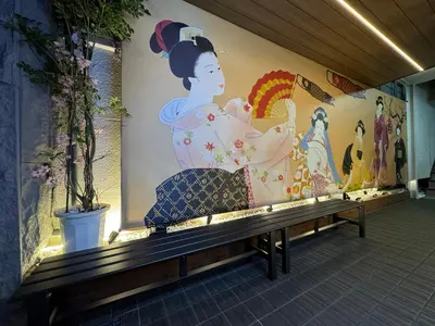 a person sitting on a bench in front of a mural at Rosenheim Tokyo Shinjuku in Tokyo