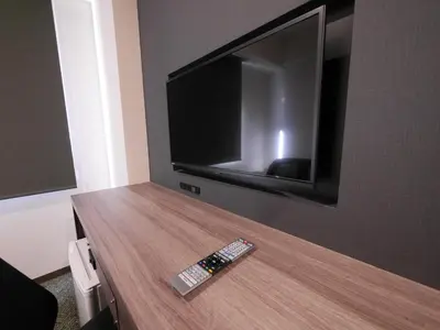 a remote control on a wooden table with a tv on a wall at Hotel Comfybed Ginza in Tokyo