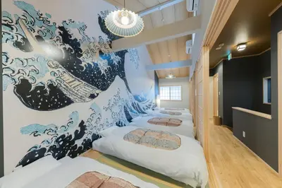 a row of beds in a room with a wave mural at YADOYA Negishi in Tokyo