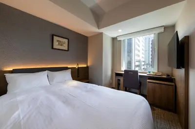 a hotel room with a bed and a desk and a window at Hotel Rilassare Tokyo in Tokyo