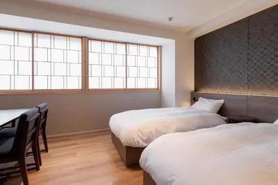 a bedroom with two beds and a table and two windows at COCOSHUKU Asakusa Kuramae in Tokyo