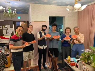 a group of people holding up slices of watermelon at Tokyo Guest House 2020 in Tokyo