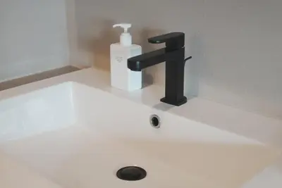 a sink with a black faucet and a bottle of soap at ICHIYU HOTEL ASAKUSA in Tokyo