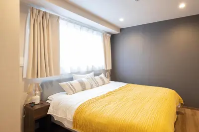 a bedroom with a bed with a yellow blanket and a window at Ken's Place麻布East in Tokyo