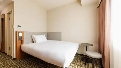 a bedroom with a large white bed and a stool at JR-East Hotel Mets Komagome in Tokyo