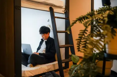 a man sitting on a bunk bed using a laptop at unito light SHIMBASHI in Tokyo