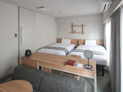 a room with two beds and a desk with a couch at Vessel Inn Asakusa Tsukuba Express in Tokyo