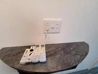 three remote controls sitting on a table next to a lightswitch at \u30d1\u30fc\u30ea\u30fc\u30d5\u30e9\u30c3\u30c4\u54c1\u5ddd\u9ad8\u8f2a\u53f0 PEARLY FLATS Shinagawa Takanawadai in Tokyo